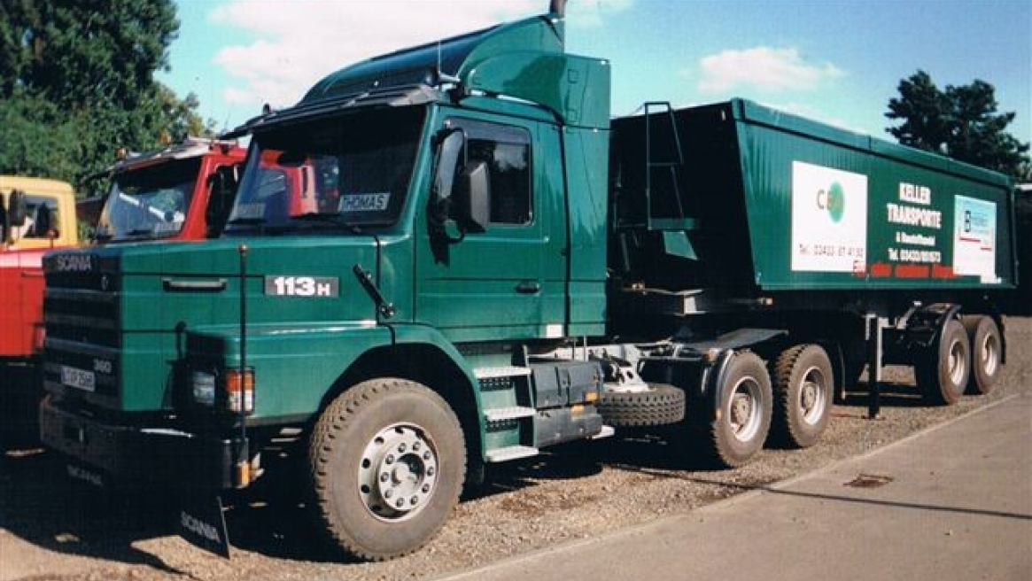 Ein grüner Scania 113H LKW mit einem Anhänger von KELLER TRANSPORTE, geparkt an der Straße unter einem klaren blauen Himmel.