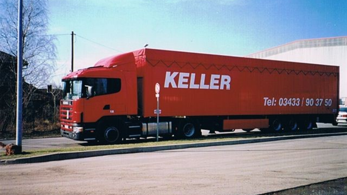 Ein roter Planen-LKW mit der Aufschrift "KELLER" in einem Industriegebiet.
