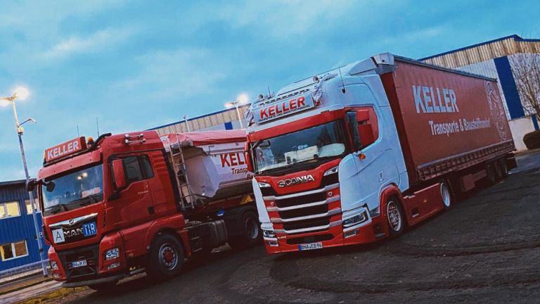 Roter LKW mit weißem Kipper-Anhänger und weißer LKW mit rotem Planenanhänger mit der Aufschrift "KELLER Transporte & Baustoffhandel" stehend in einem Industriegebiet.